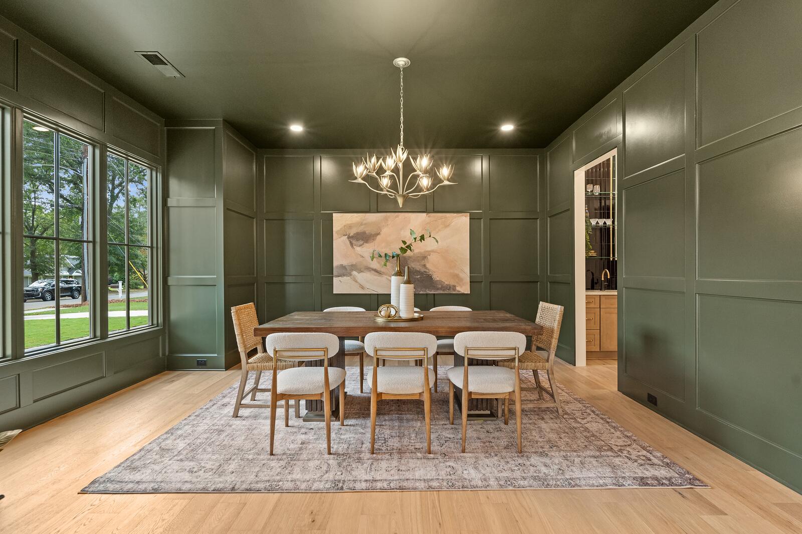 A dining room in deep green with painted paneling and a chandelier