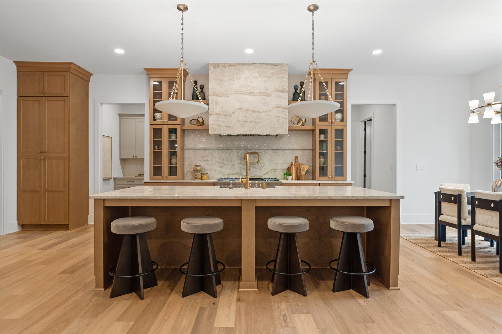 A finished kitchen with oak cabinetry, a brass-trimmed hood, and an island with stools
